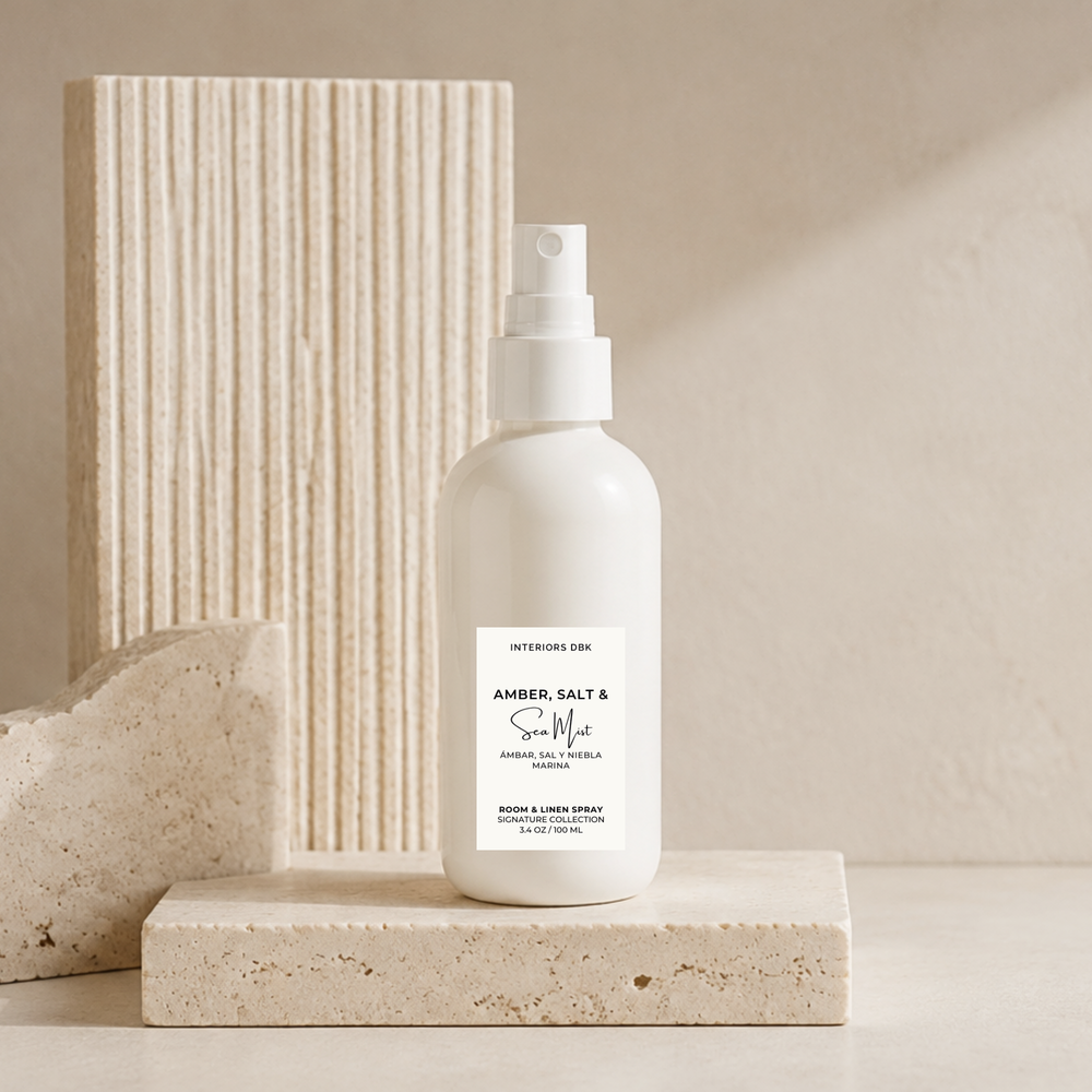 A scented room and linen spray in a white glass bottle. Amber, Salt & Sea Mist by Interior Design, a luxury home fragrance, styled on a textured stone block with a ribbed beige block in the background.