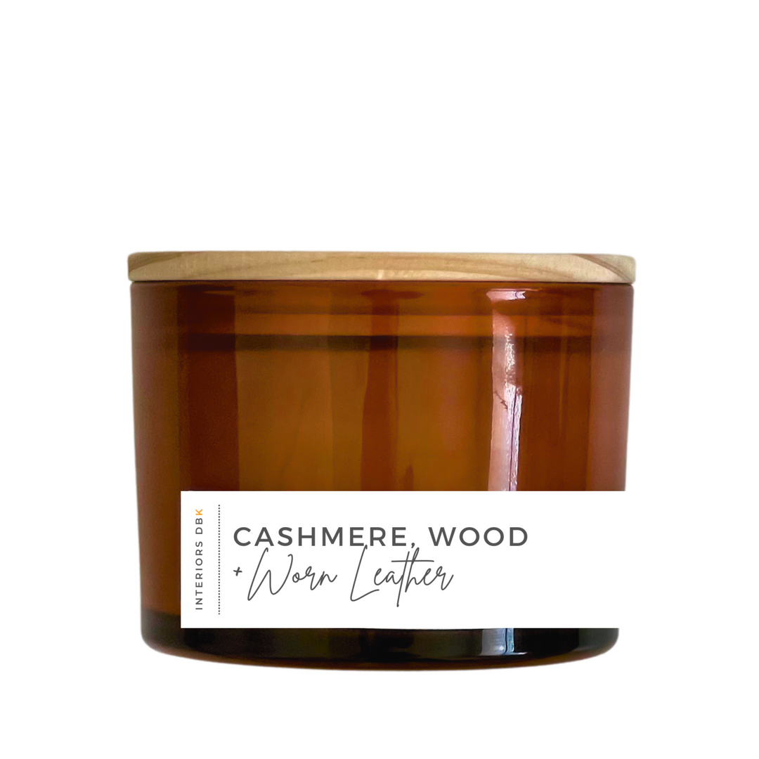 A large Cashmere, Wood & Worn Leather soy candle in an amber glass vessel with a natural wood lid, featuring a 12 oz volume and a sophisticated, sustainable design.