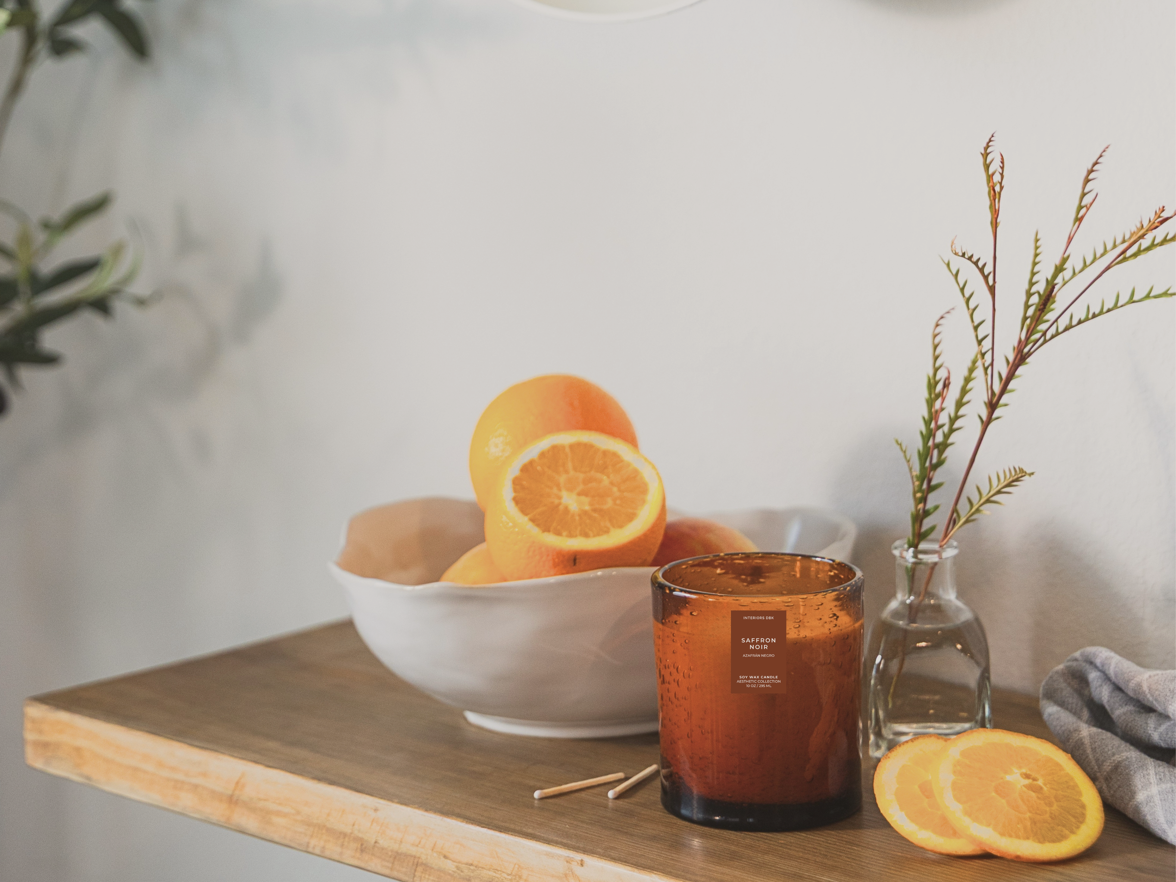 Soy wax candle by Interiors DBK styled with oranges and greenery on a wooden surface.
