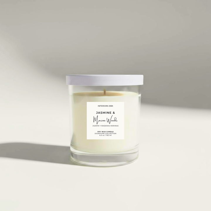 Jasmine & Marine Woods 6.5 oz soy candle by Interiors DBK in clear glass vessel with white metal lid.