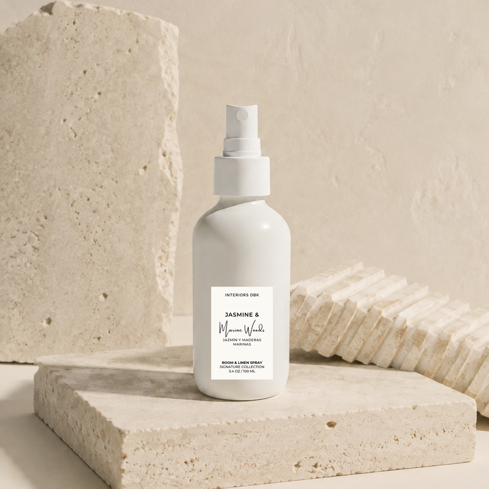 Jasmine and Marine Woods room and linen spray. A matte white spray bottle by Interiors DBK stands centered on a textured stone slab, with matching stone props in the background.
