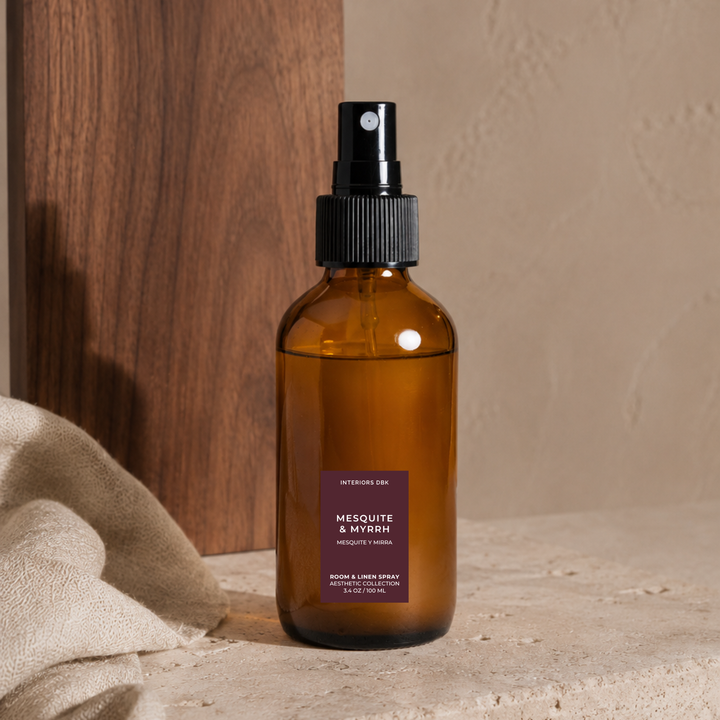 Mesquite and Myrrh by Interiors DBK. Set on a stone surface with a draped beige cloth and a wooden panel in the background.